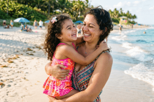 Mother and daughter share a warm hug and big smiles on a sunny beach by the sea touch.