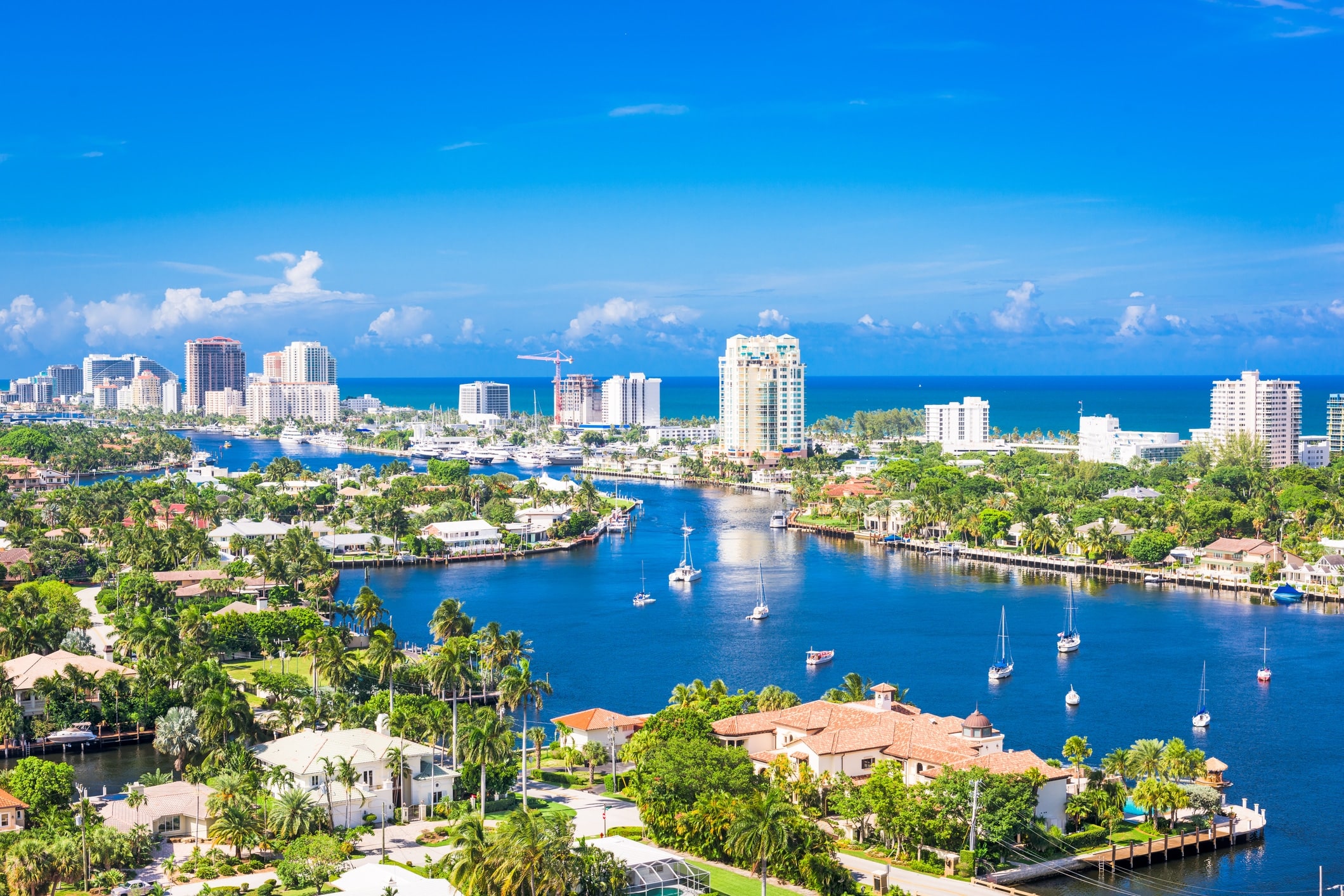 Fort Lauderdale South Florida Sunny coastal city with high-rise buildings along a marina and palm trees, blue sea in the background