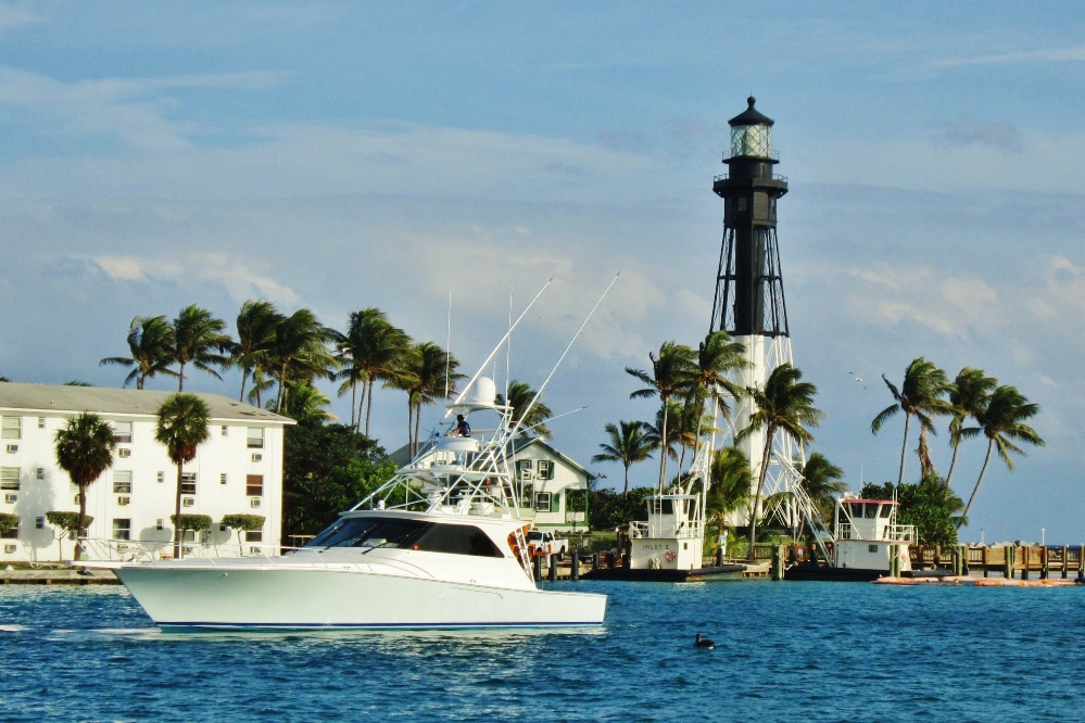 Lighthouse Pointe, FL Sunny coastal city with high-rise buildings along a marina and palm trees, blue sea in the background