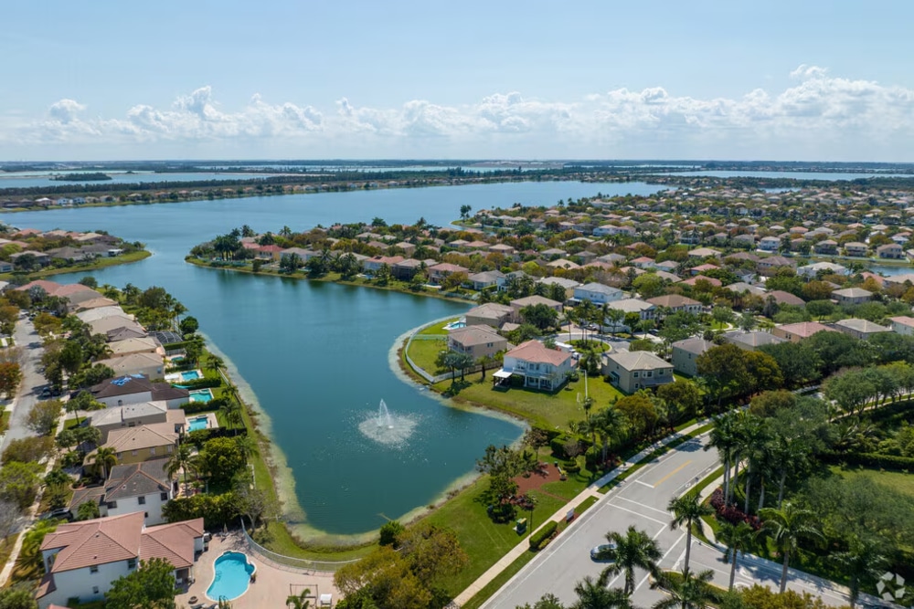 Sunny coastal city with high-rise buildings along a marina and palm trees, blue sea in the background