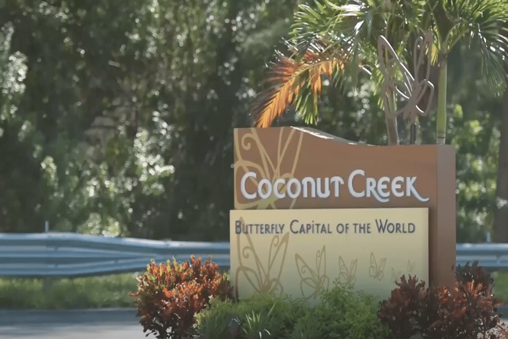Coconut Creek Sunny coastal city with high-rise buildings along a marina and palm trees, blue sea in the background