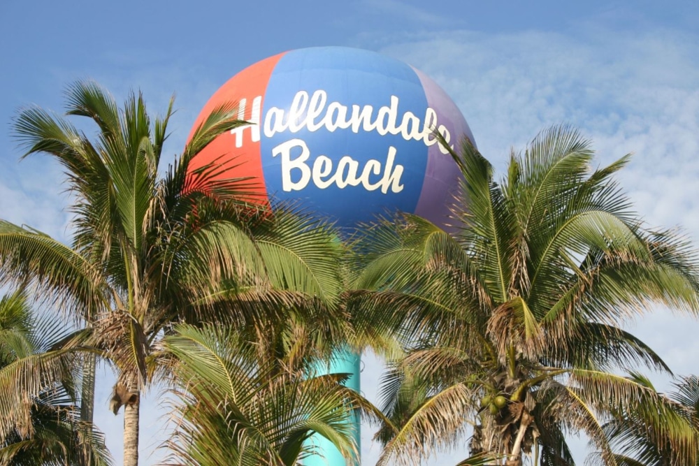 Sunny coastal city with high-rise buildings along a marina and palm trees, blue sea in the background