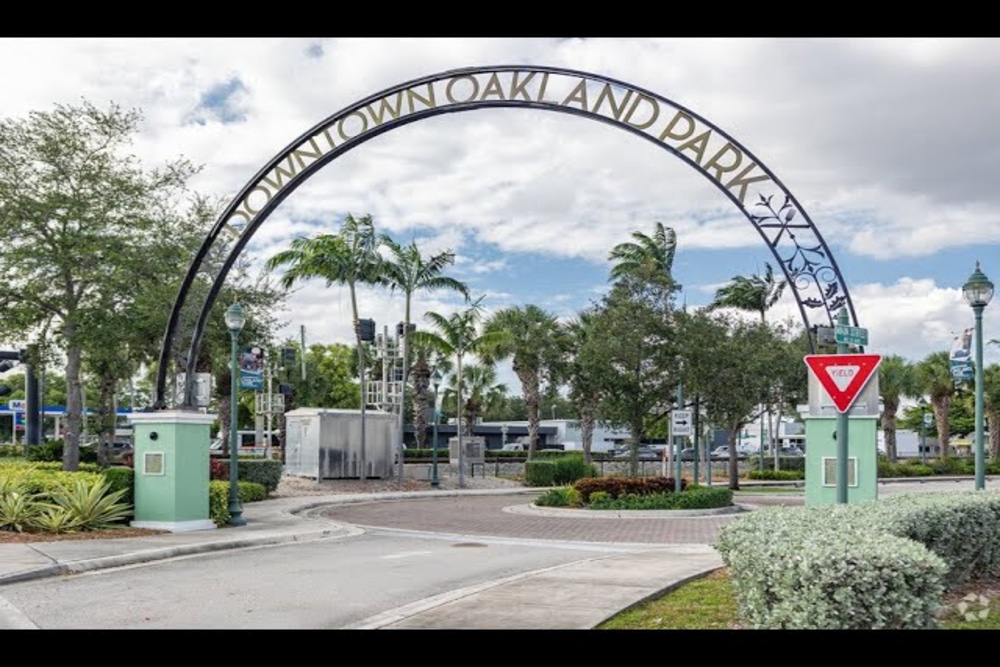 Oakland Park Sunny coastal city with high-rise buildings along a marina and palm trees, blue sea in the background