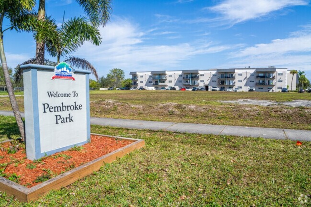 Sunny coastal city with high-rise buildings along a marina and palm trees, blue sea in the background